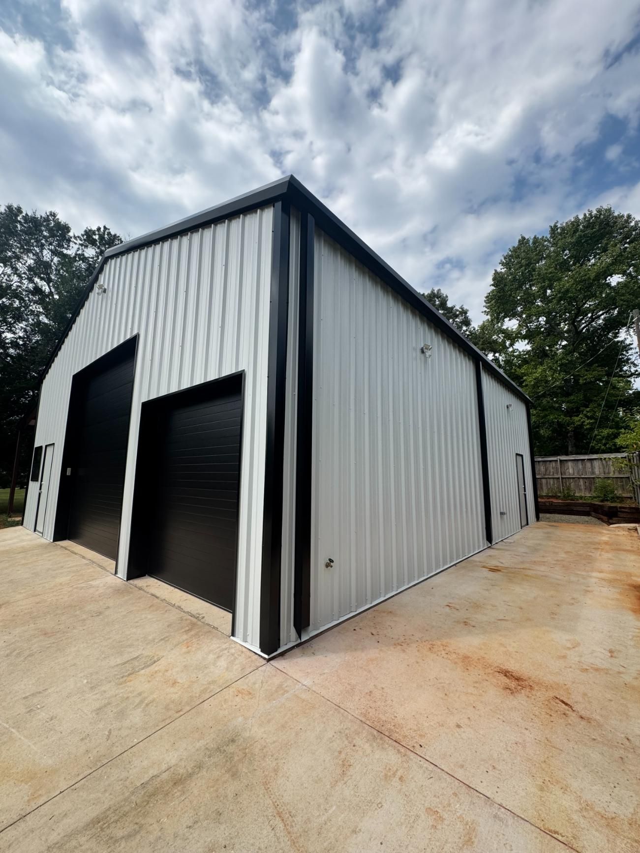 Two-bay metal barn with black doors and trim, on a concrete pad.