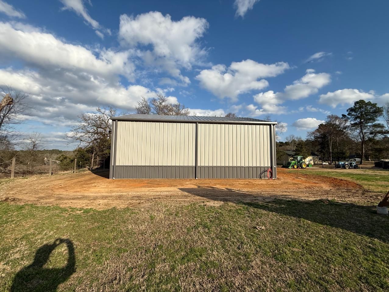 Metal shed on a dirt patch against a blue sky with clouds; green grass in the foreground.