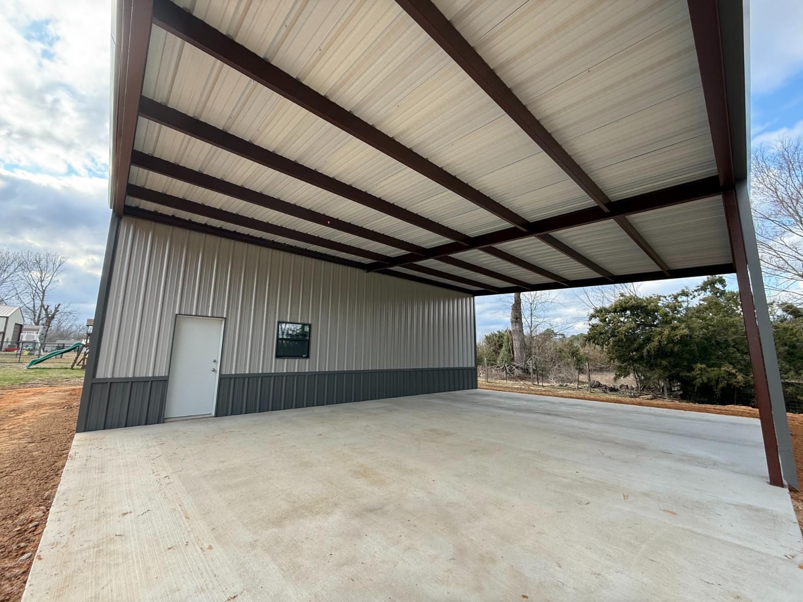 Steel carport with concrete floor and metal siding; brown trim.
