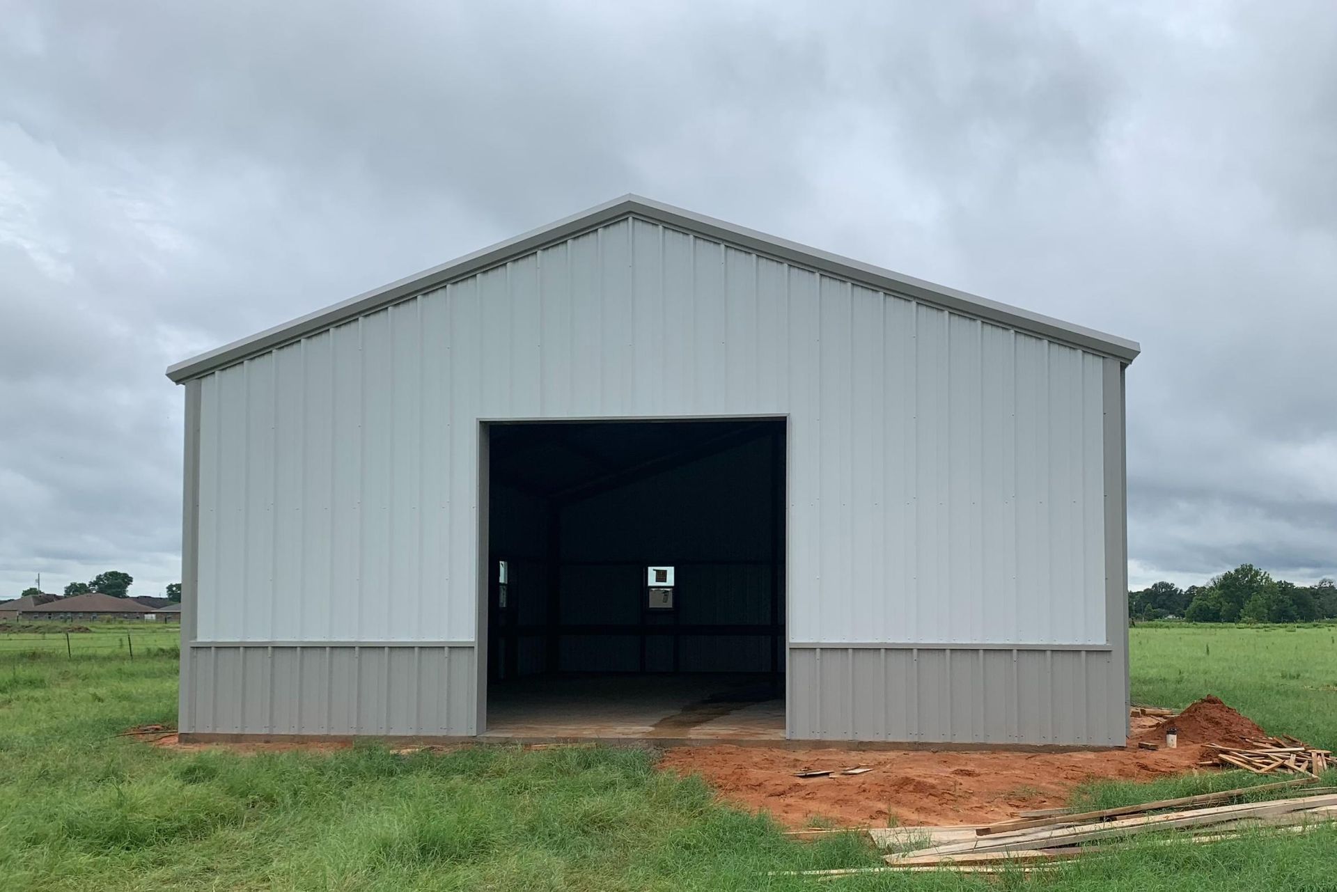 Metal barn with an open door in a field under a cloudy sky.