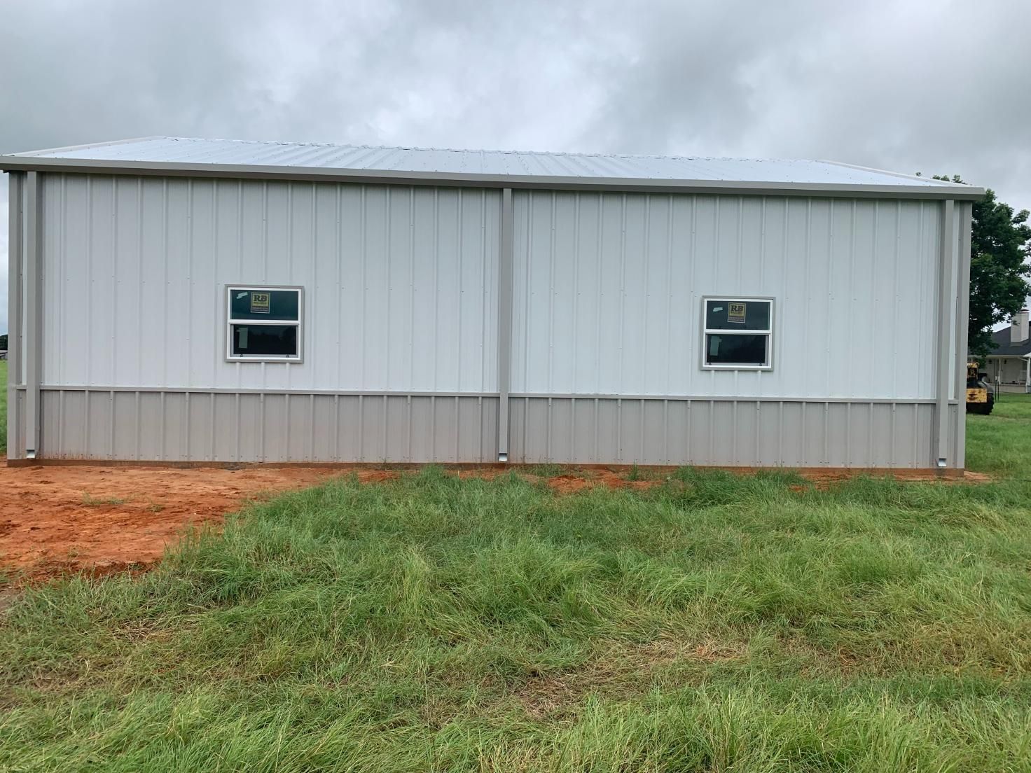 White and tan metal building with two small windows, set on a grassy lot.