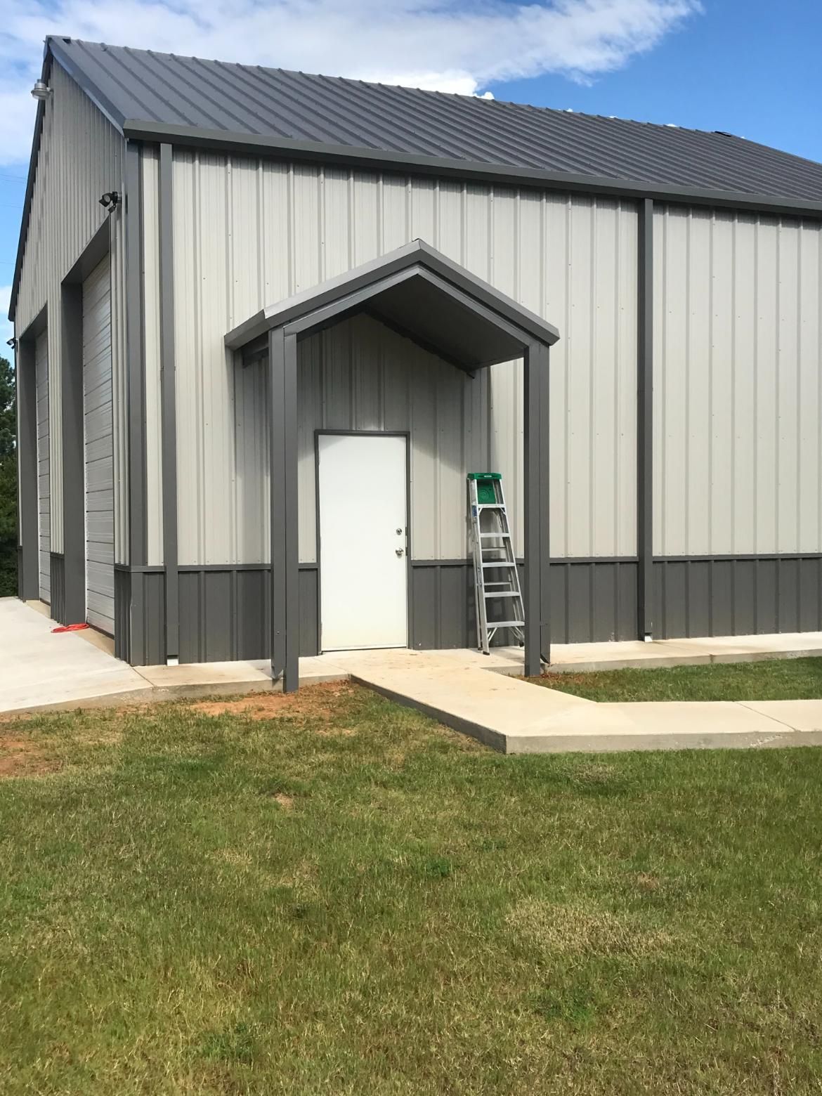 Gray metal building with a doorway under a small awning. A ladder leans against the building.