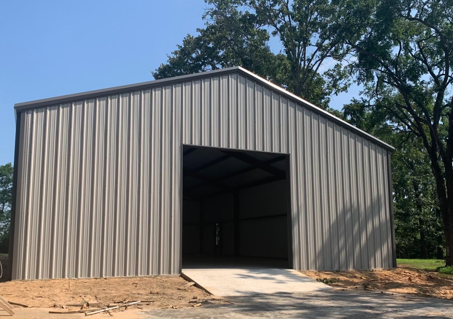 Metal barn with open doorway and concrete ramp, set against a blue sky and trees.