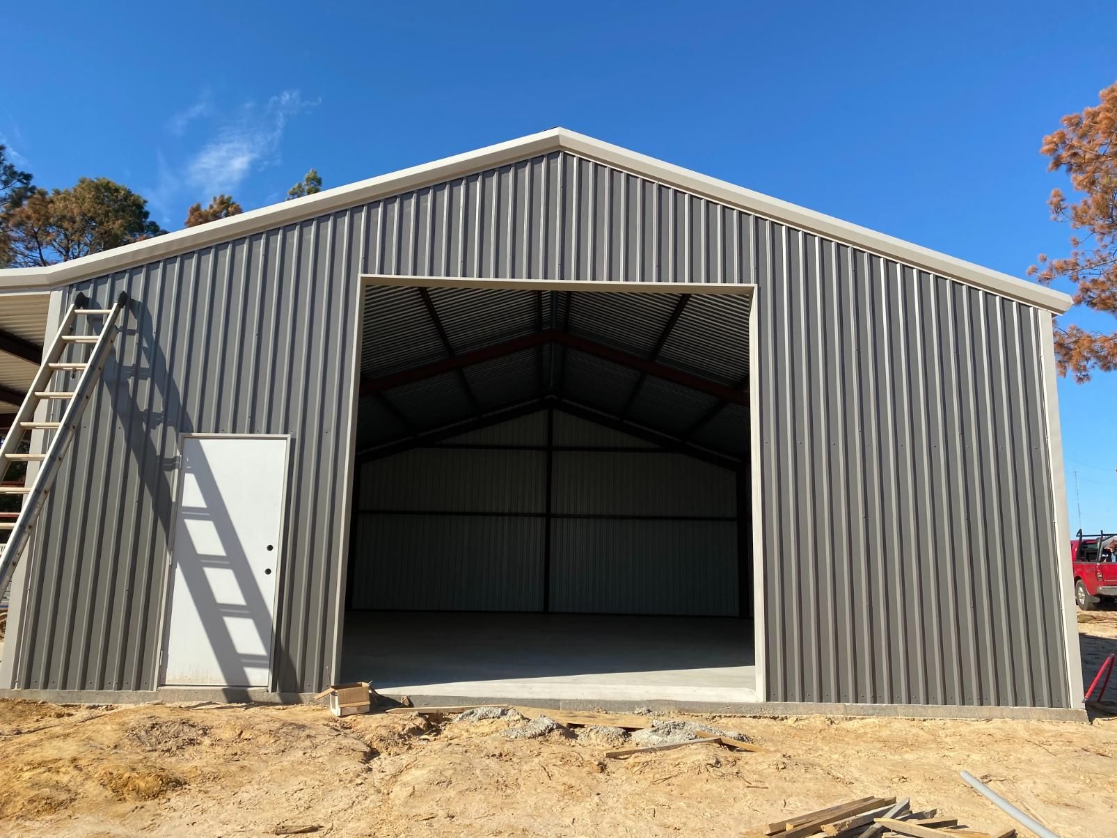 Steel building with open entrance and side door; constructed against a blue sky.