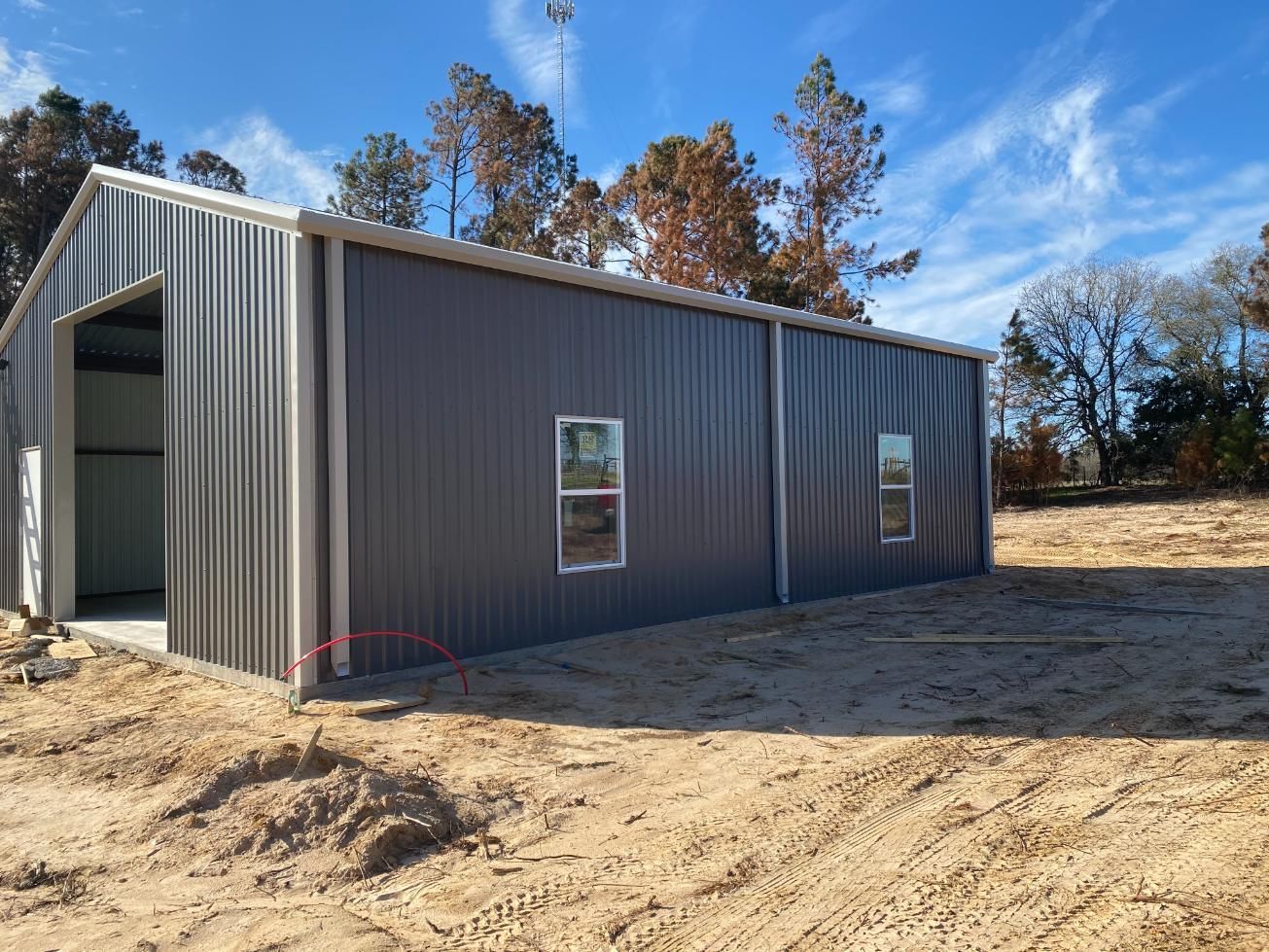 Gray metal building under construction with windows, on a sunny day.