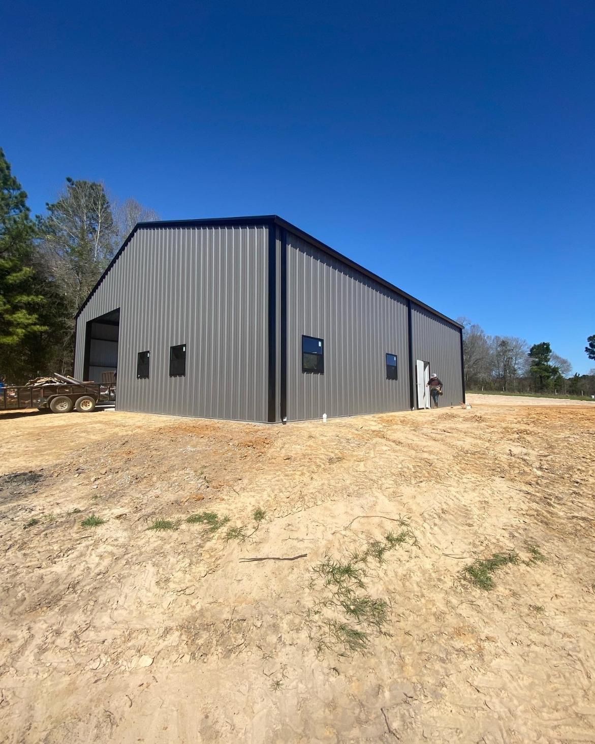 A large metal building with black trim on a sunny day in a rural setting.