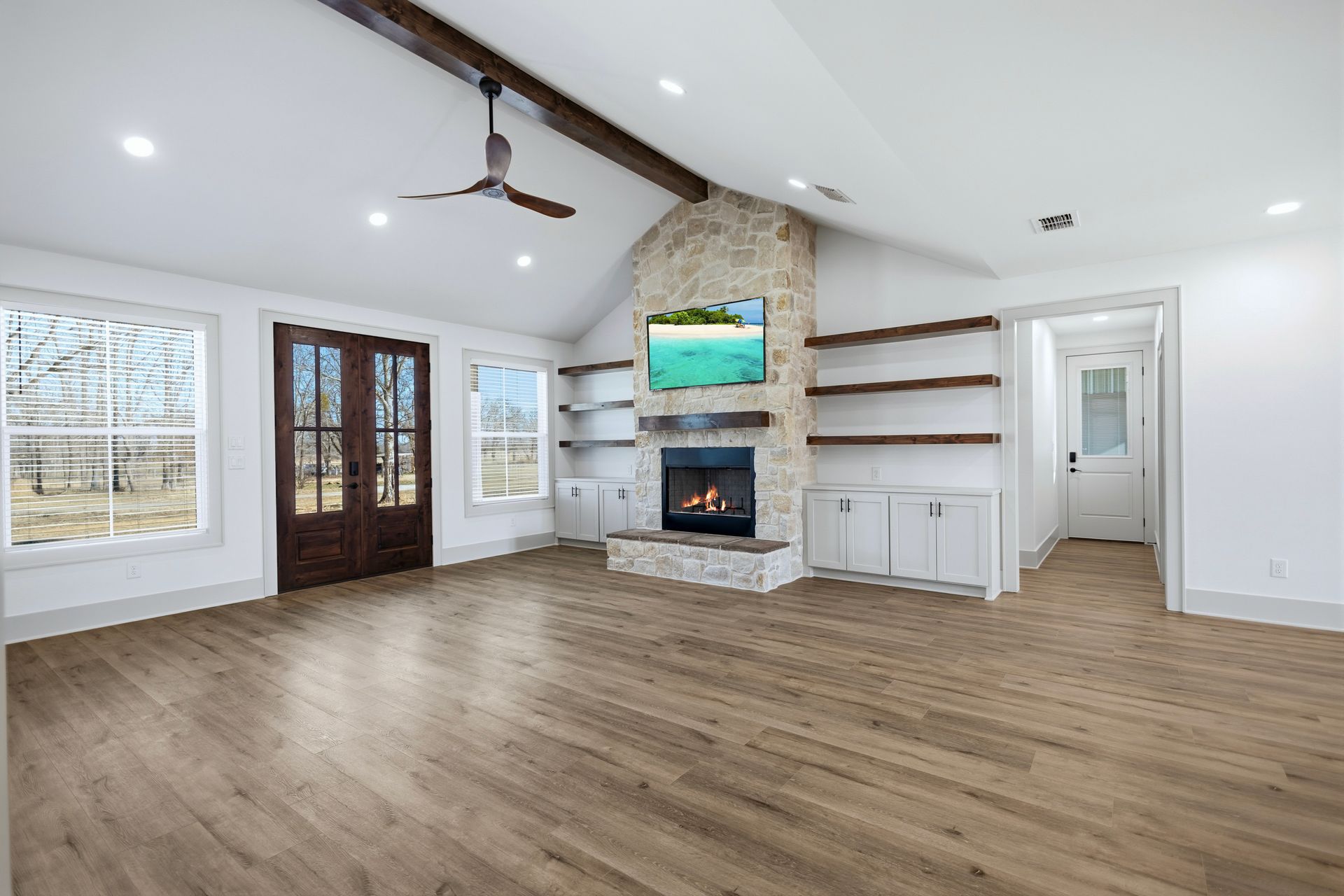 Modern living room with a kitchen. Light wood floors, white walls, fireplace, and a TV.