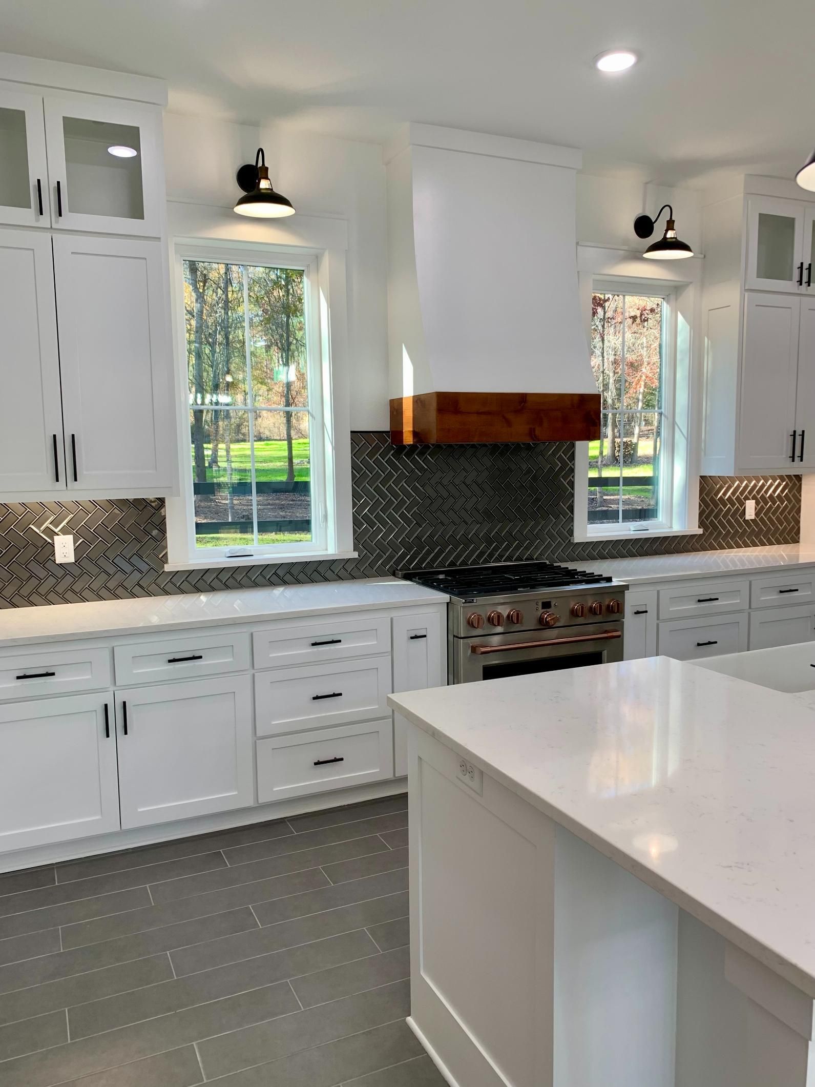 White kitchen with stove, cabinets, windows, and island. Black and white tile backsplash, stainless steel appliances.