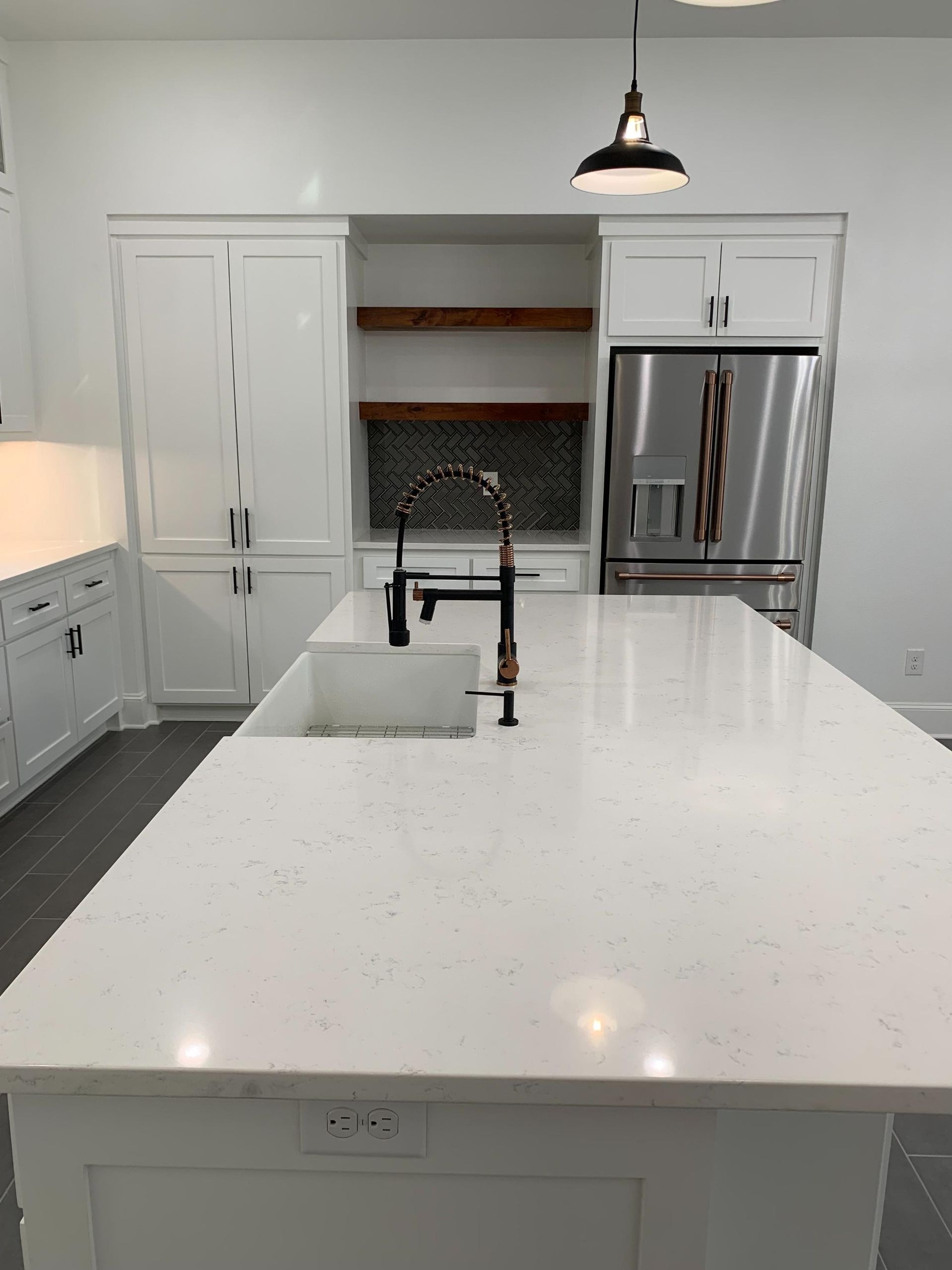 White kitchen island with black faucet, white cabinets, stainless steel refrigerator, and wooden shelves.