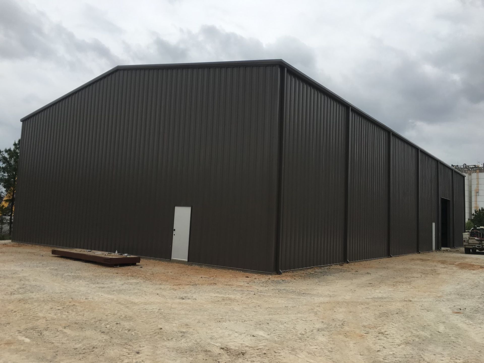 Dark brown metal warehouse building with a small white door and gray sky.