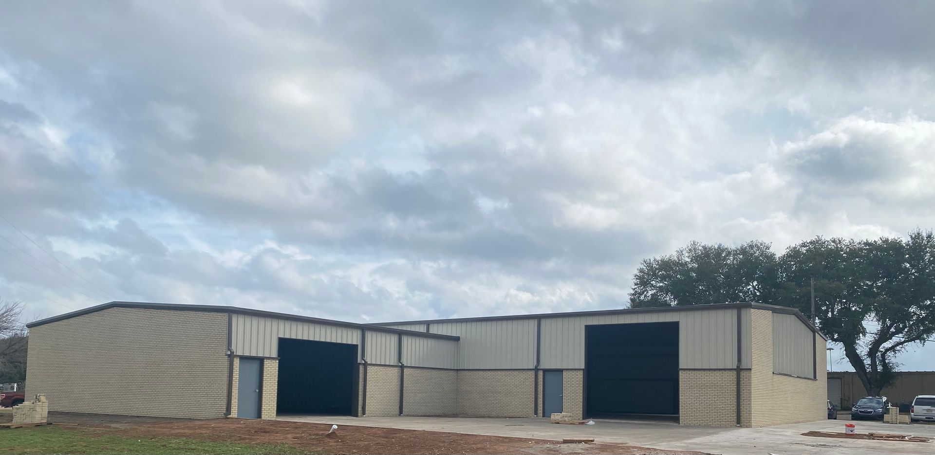 A large, light-colored metal building with black garage doors under a cloudy sky.