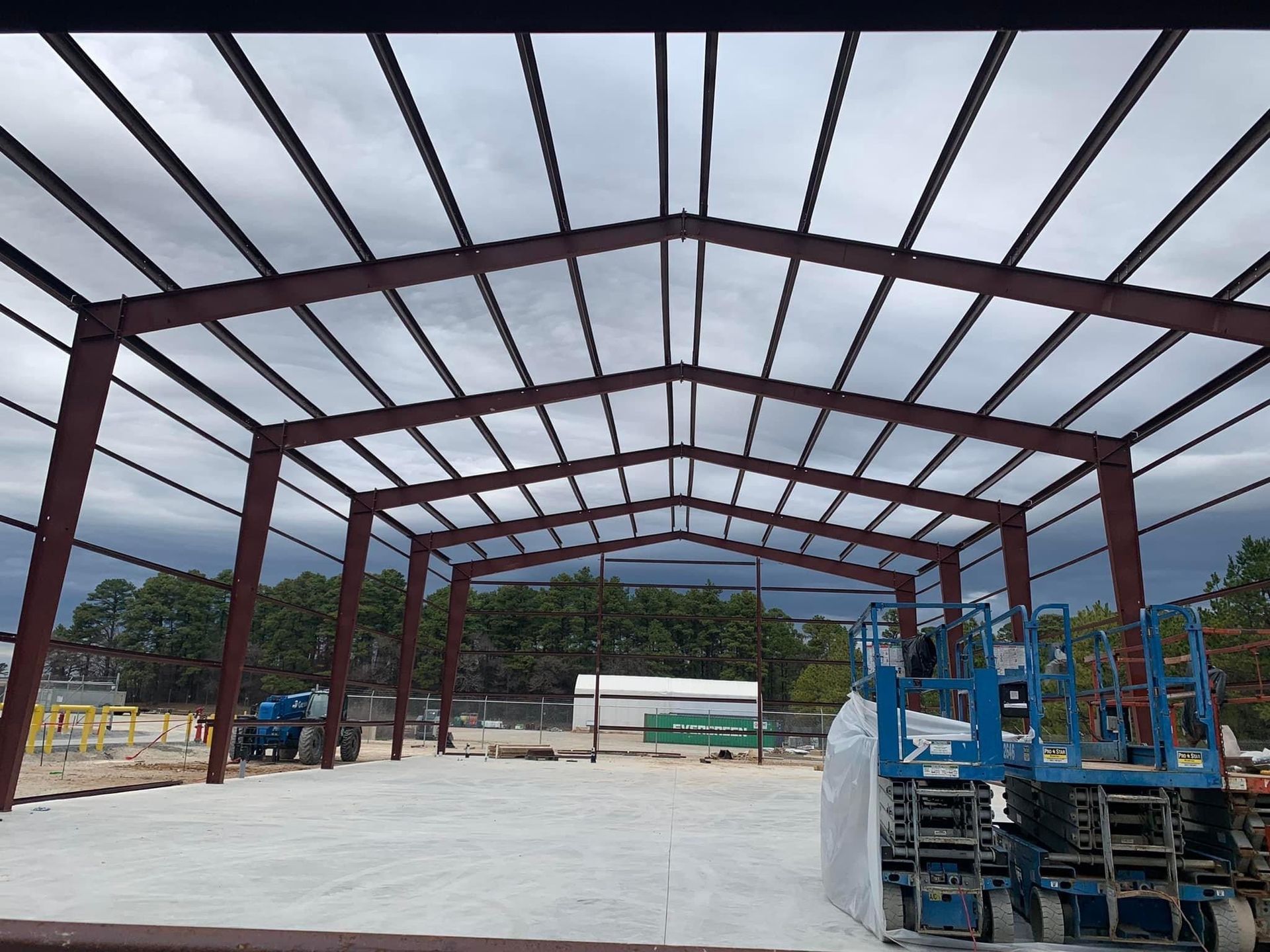 Steel frame of a building under construction; red beams, blue lift, cloudy sky.
