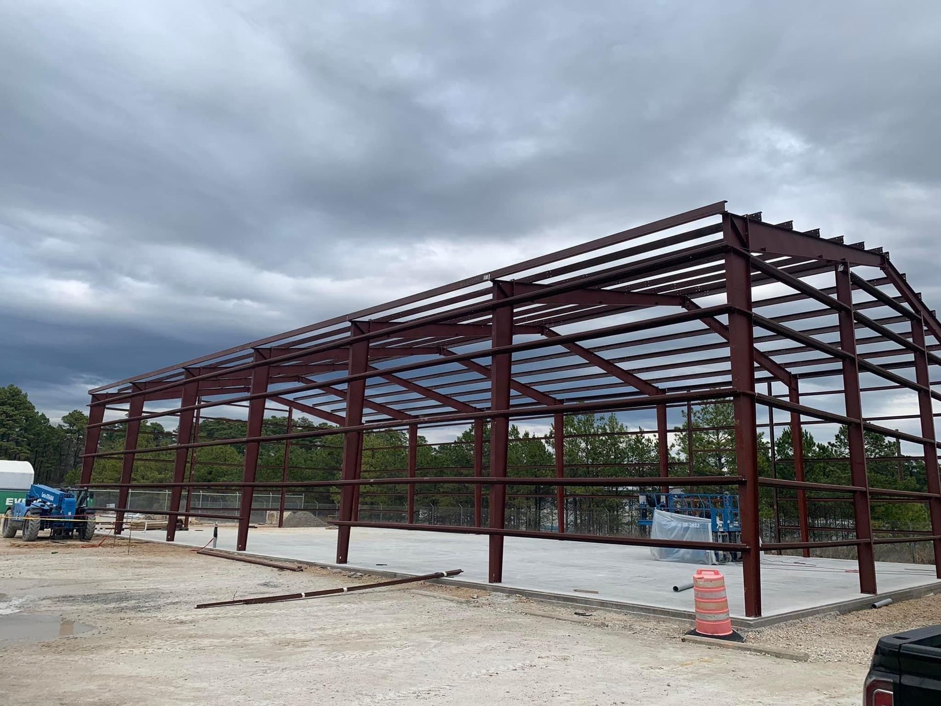 Steel frame construction of a building with a concrete base under a cloudy sky.
