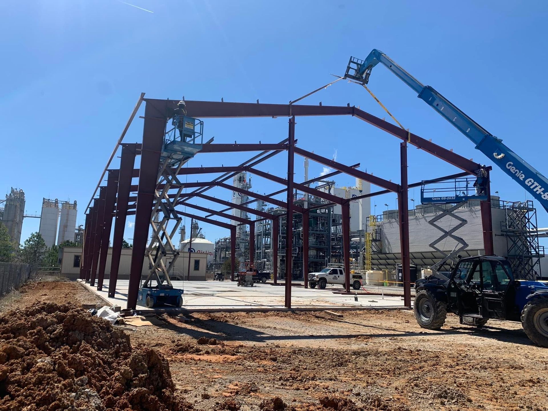 Steel frame of a building being constructed with a lift, against a blue sky.