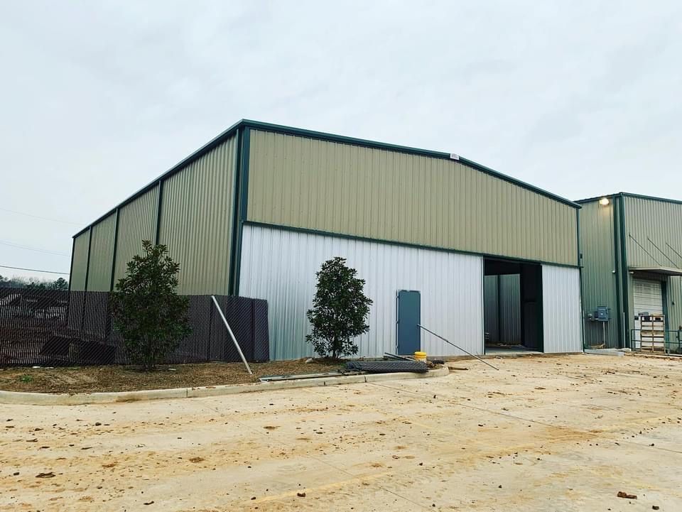 Large metal warehouse with beige and white panels, open sliding door, trees in front.