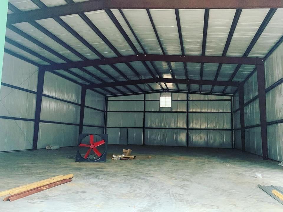 Empty metal building with spray foam insulation; a large fan sits on the floor.