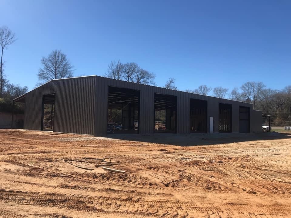 Metal building under construction; brown exterior, open bays, on a dirt lot.