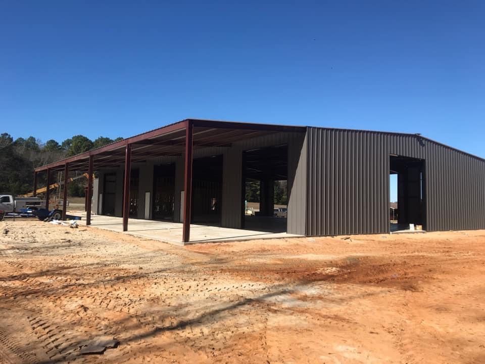 Brown metal building under construction with a covered porch on a dirt lot.