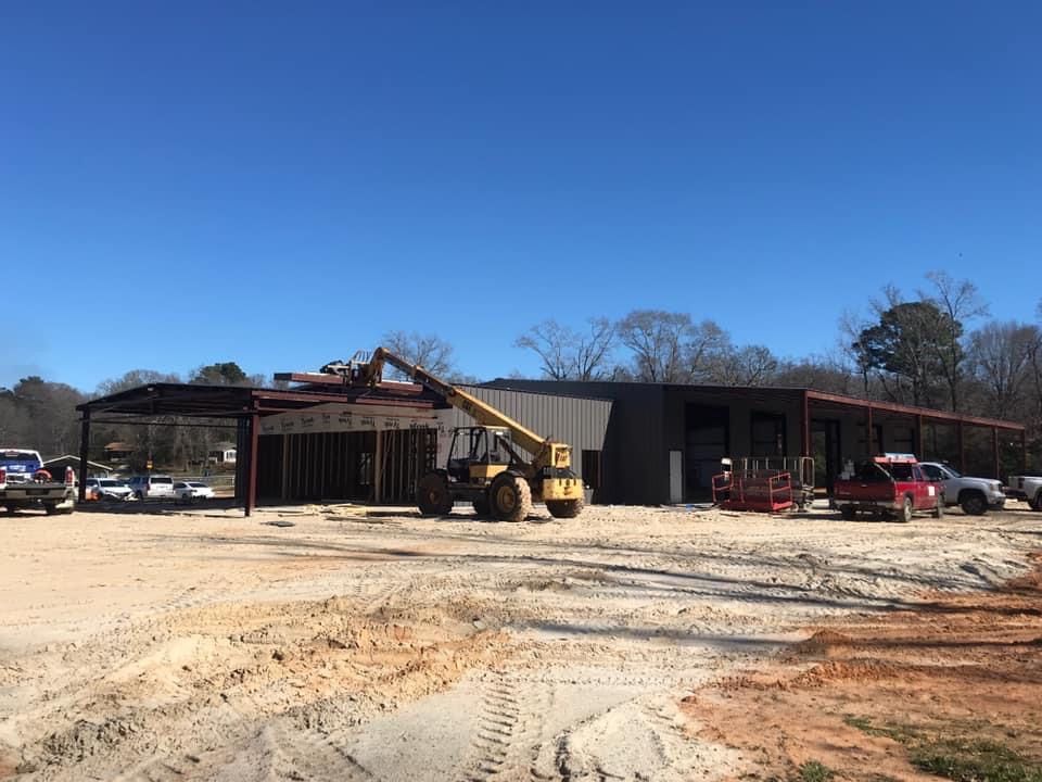 Construction of a metal building on a sunny day; a yellow forklift lifts materials.