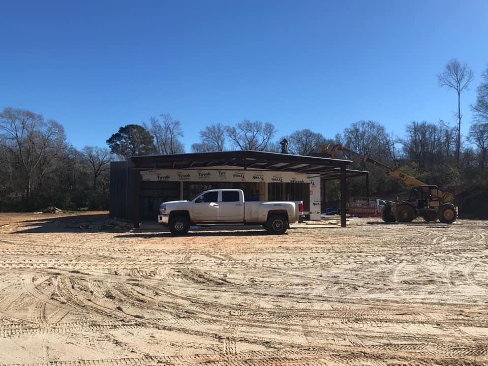 Construction site with a white truck parked in front of a partially built building; a front-end loader sits to the side.