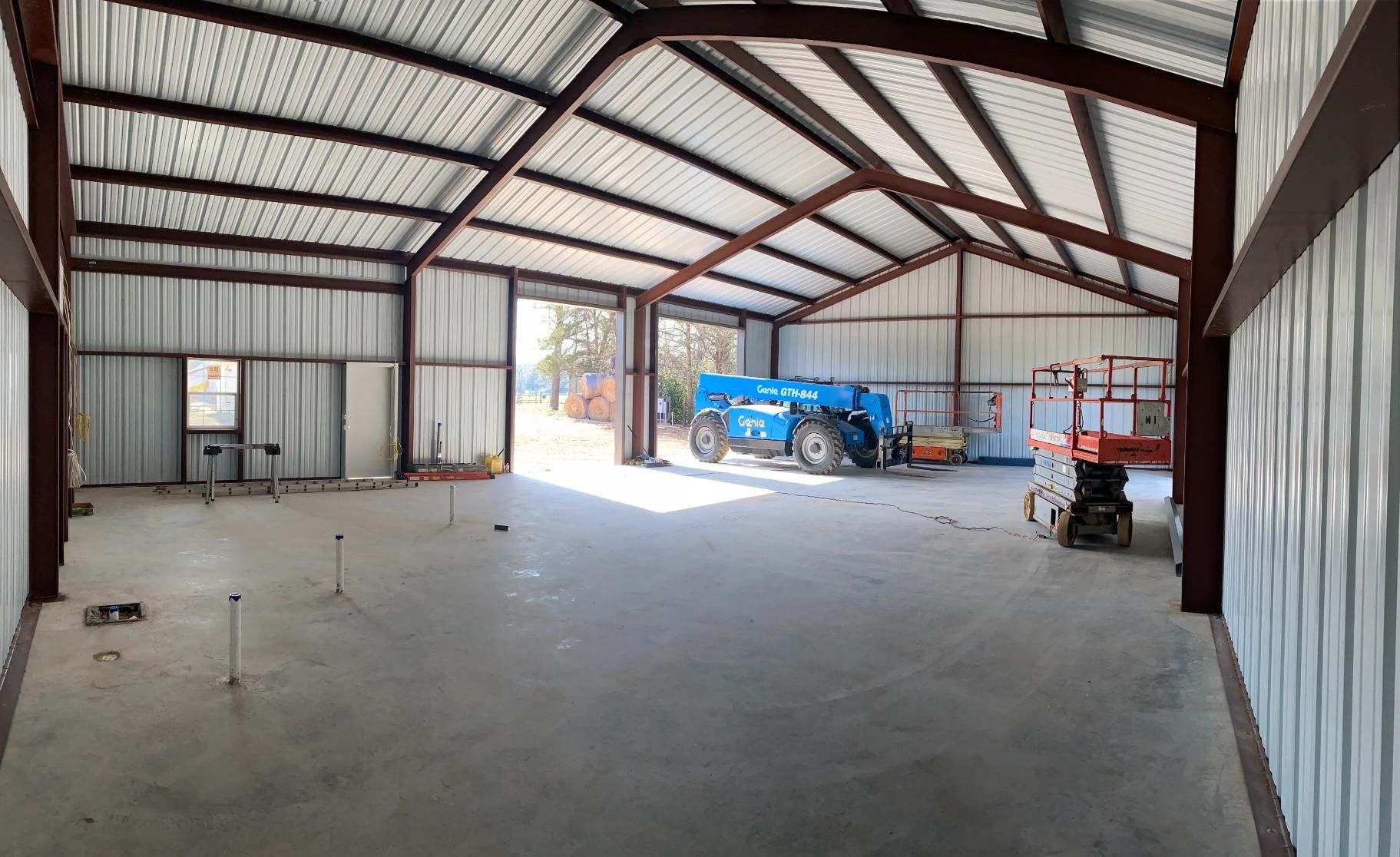 Wide interior view of a large metal-framed building with concrete floor; tractor, lift, and doors.