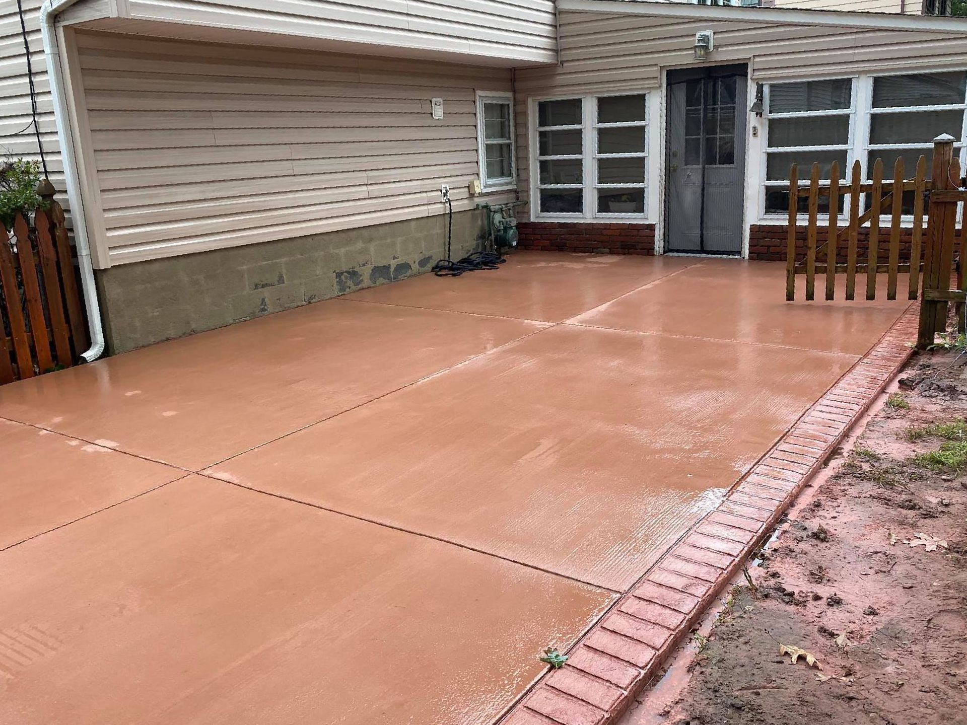 A custom colored concrete driveway in front of a house with a wooden fence.