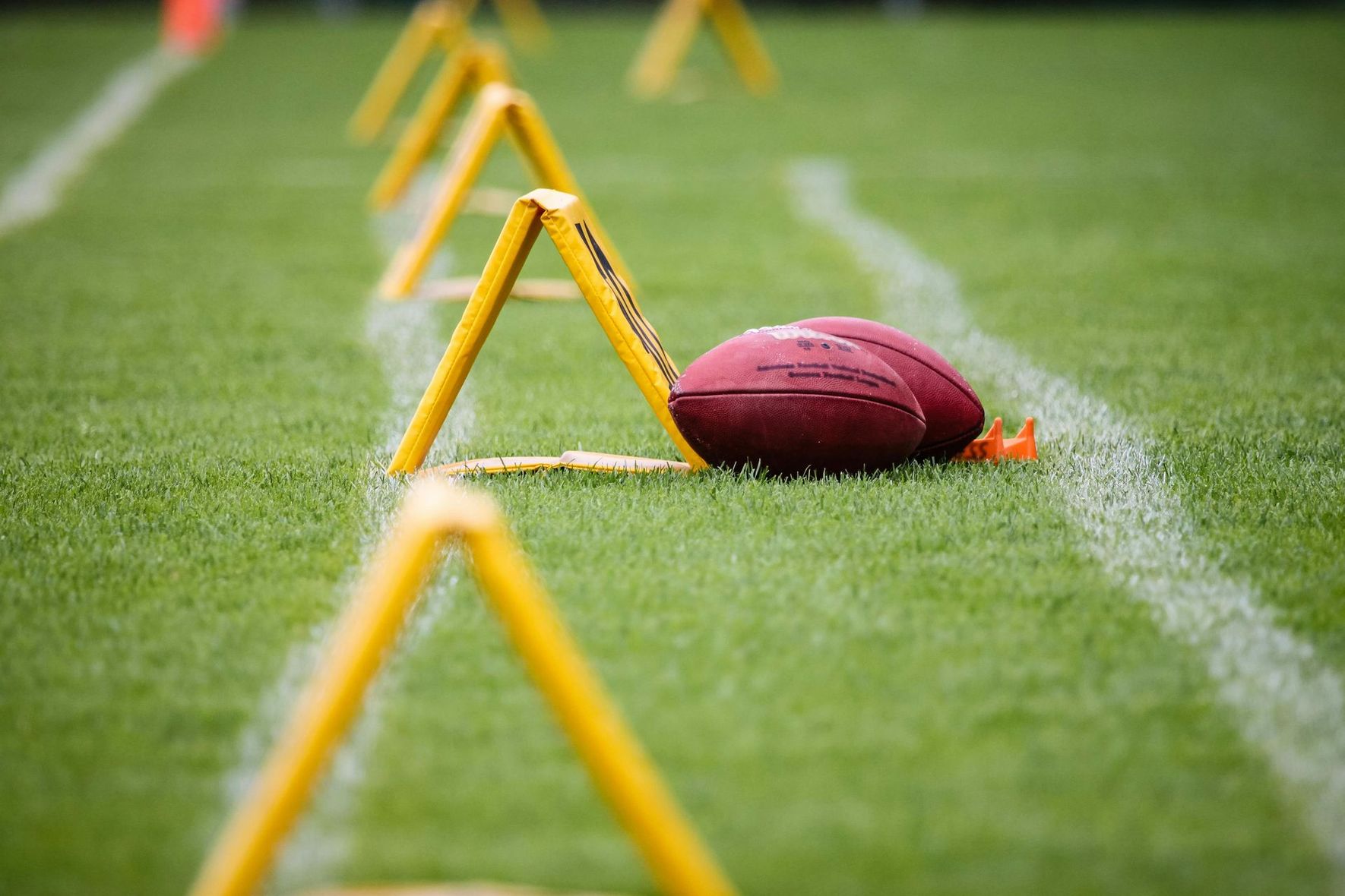 Football on green turf with yellow training markers and a ball near a white sideline