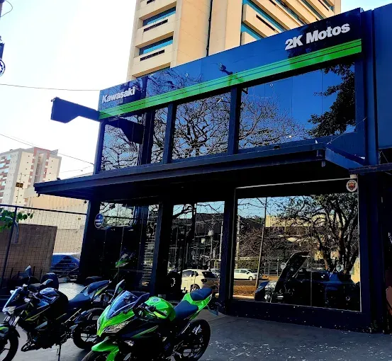 Concessionária de motocicletas "2K Motos" com motos Kawasaki estacionadas do lado de fora. Detalhes em azul e verde.