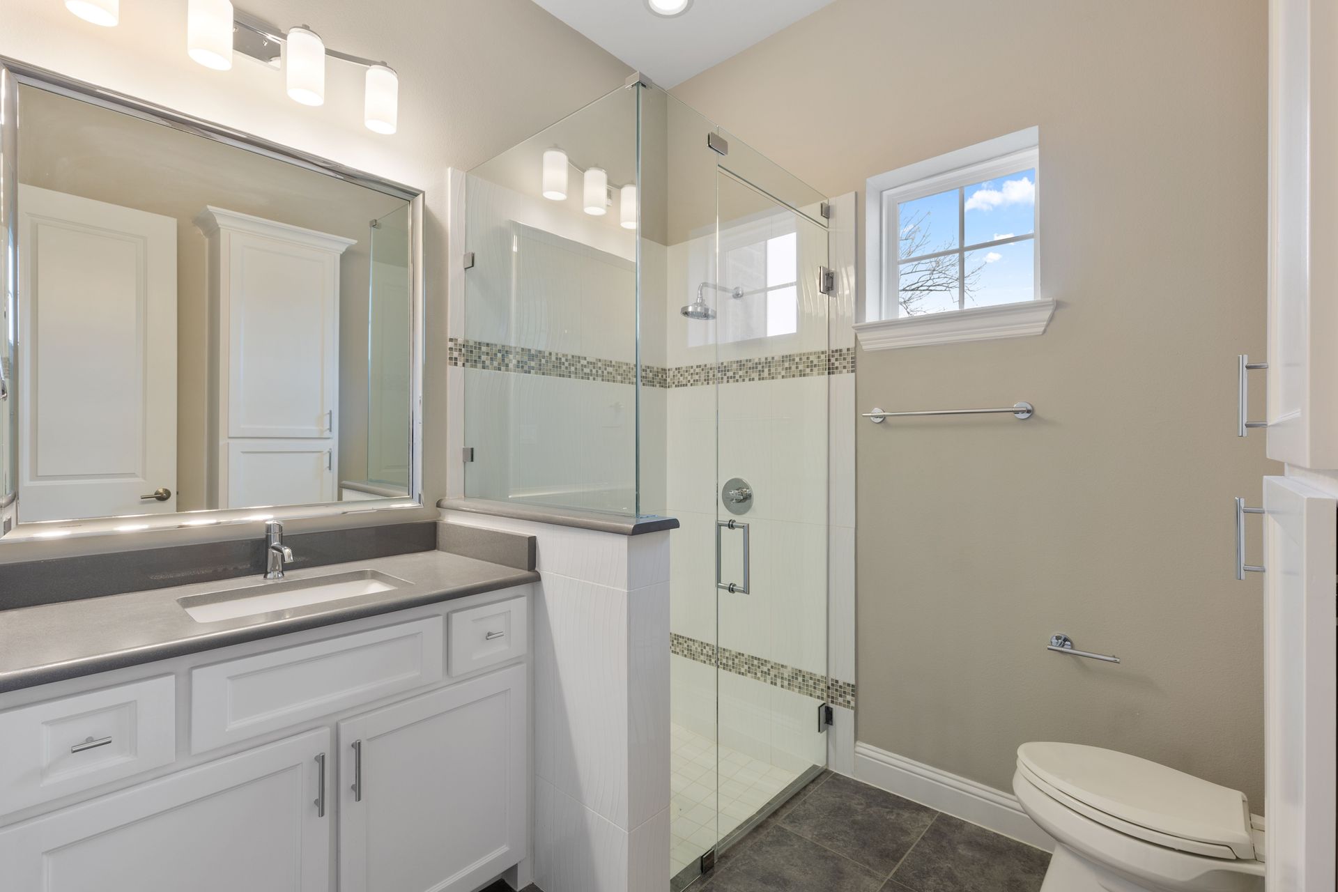 A bathroom with a toilet, sink, mirror and walk in shower.