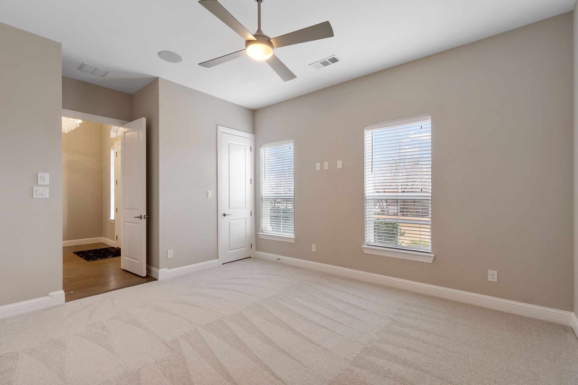 An empty bedroom with a ceiling fan and two windows.