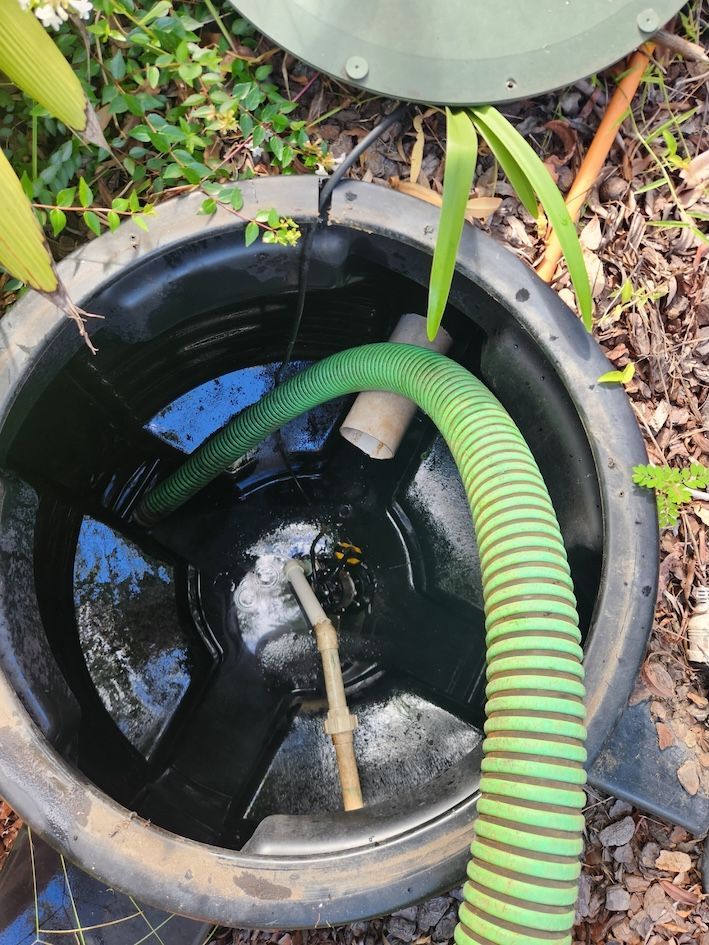 Black plastic container with water and a green hose, set outdoors— Landsborough Septic Services in Landsborough, QLD