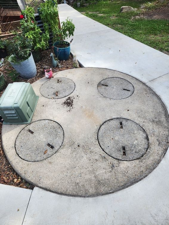 Concrete utility cover with four access lids, a green box, and plants next to a sidewalk — Landsborough Septic Services in Landsborough, QLD