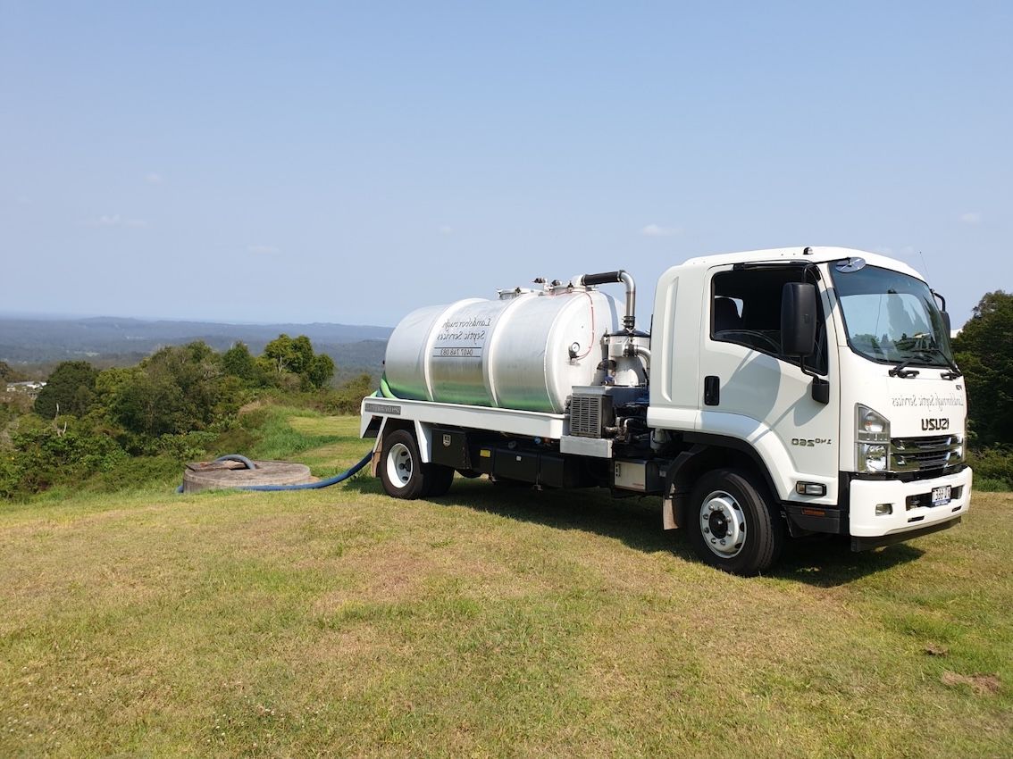 White septic tank truck on a grassy hill; hose connected to a ground-level opening, blue sky in the background— Landsborough Septic Services in Landsborough, QLD