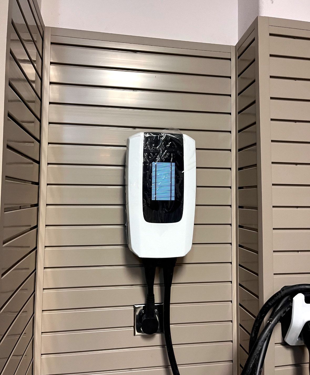 A white electric car charger is hanging on a wall.