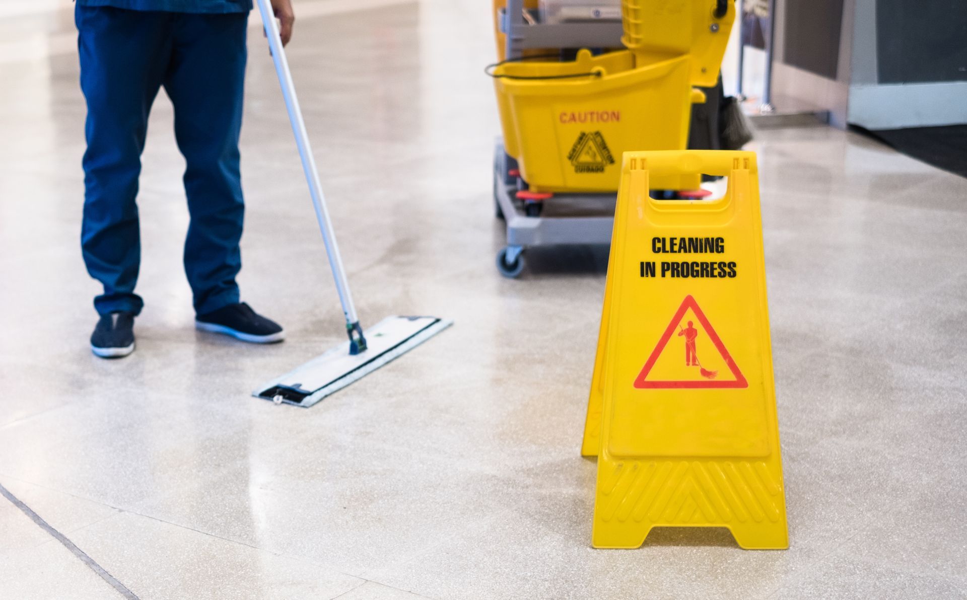 Yellow “Cleaning in Progress” sign beside mop and bucket on polished floor.