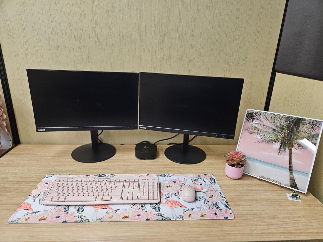 Desk setup with two monitors, pink keyboard and mouse, floral mousepad, and a decorative picture.