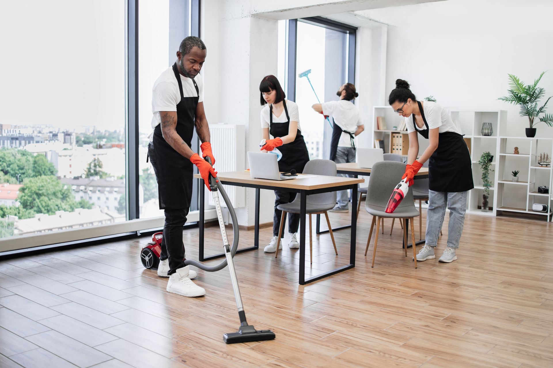 Cleaning staff vacuuming and dusting an office with large windows and wooden floors. Cleaning staff vacuuming and dusting an office with large windows and wooden floors.