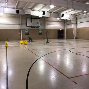 Indoor gymnasium, wet floor from cleaning; basketball hoop, buckets, and cleaning machine visible.