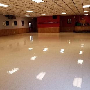 Empty dance floor with shiny, reflective surface, red and wood panel walls, and ceiling lights.