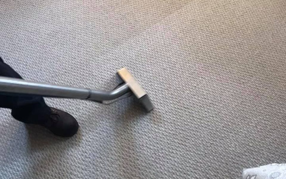 A person cleaning light-colored carpet with a carpet cleaning wand.