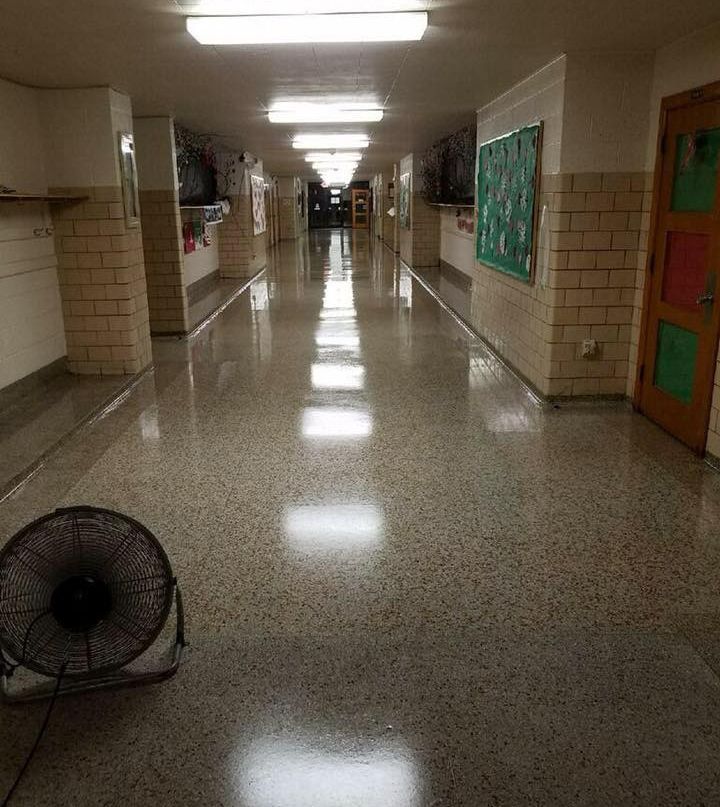 Long, empty school hallway with shiny floor, fluorescent lights, and a fan.