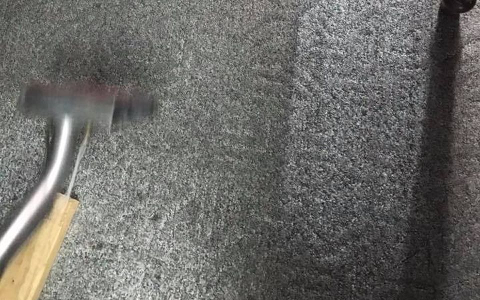 A carpet being cleaned with a steam cleaner; gray carpet with streaks from the cleaning.