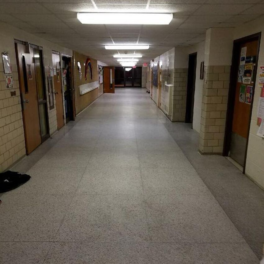 Empty school hallway with doors, fluorescent lights, and tile flooring.