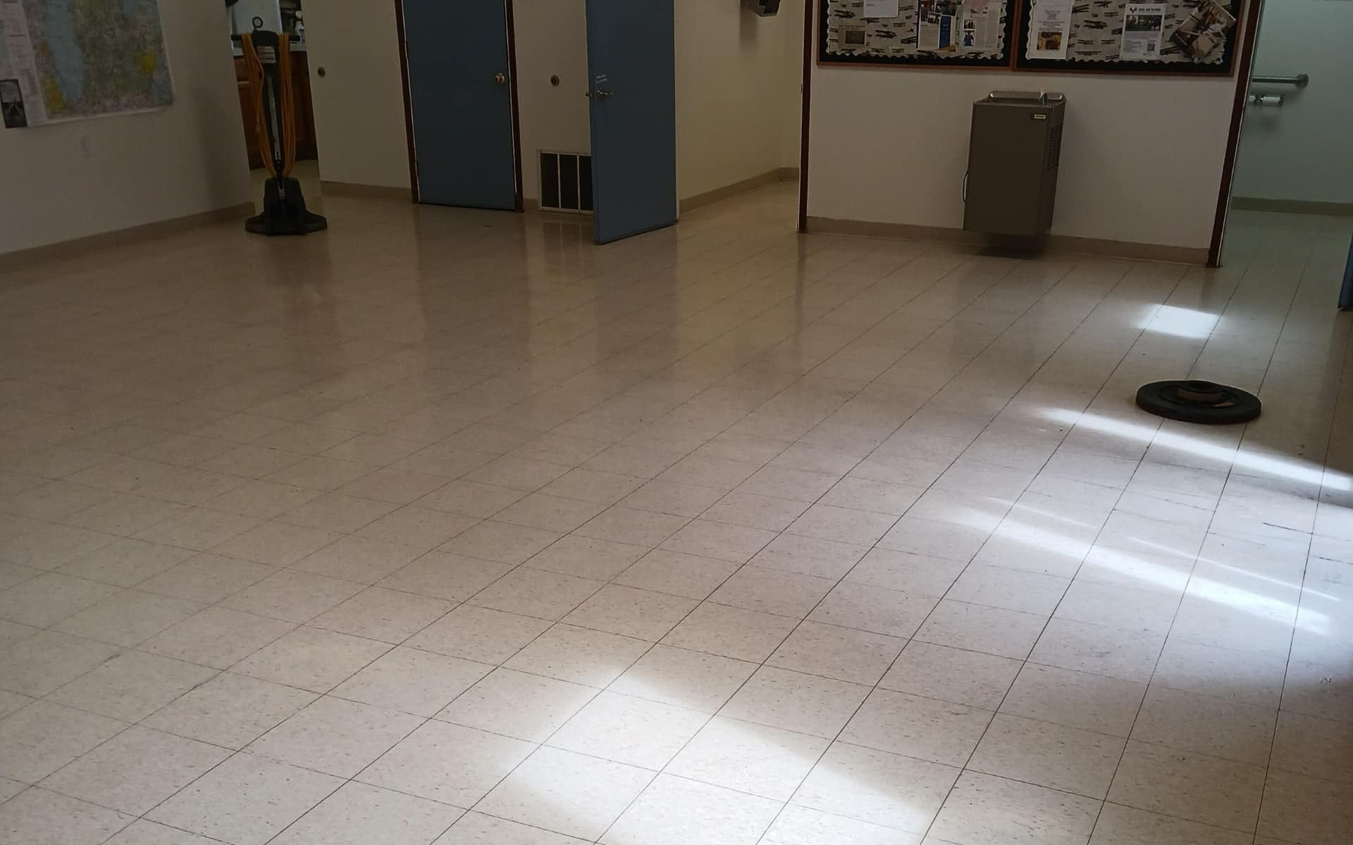 Brightly lit room with shiny tile floor. A robot vacuum and blue doors are visible.