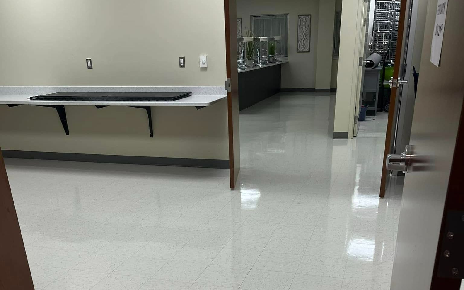 Empty hallway with white speckled floor, tan walls, and a desk against the left wall. A doorway is open on the right.
