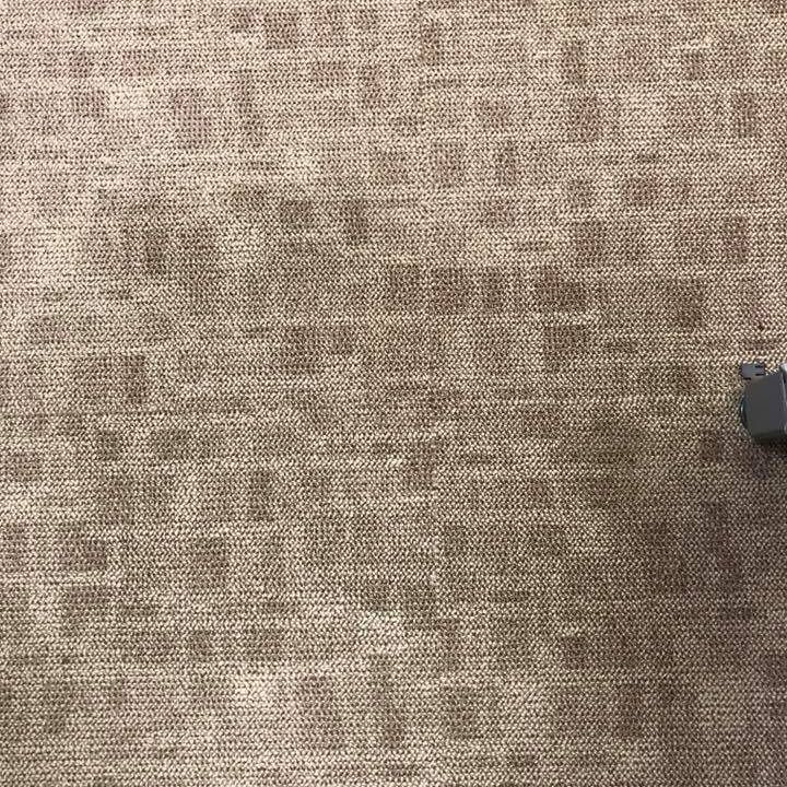 Tan carpet with a grid pattern, part of a gray object in the lower right corner.