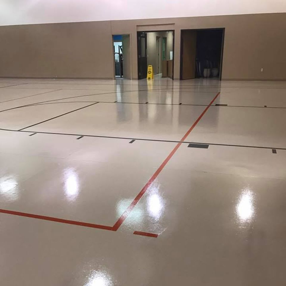 Gymnasium floor with red and black lines, leading to doorways. Light reflects off the shiny floor.