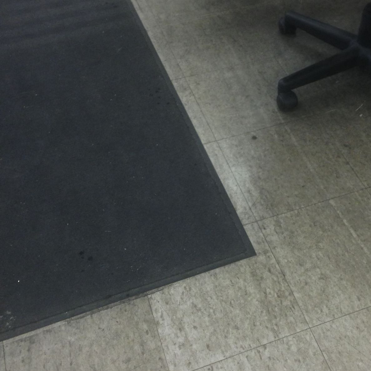Black floor mat on light-colored floor, a black chair leg is in the upper right.