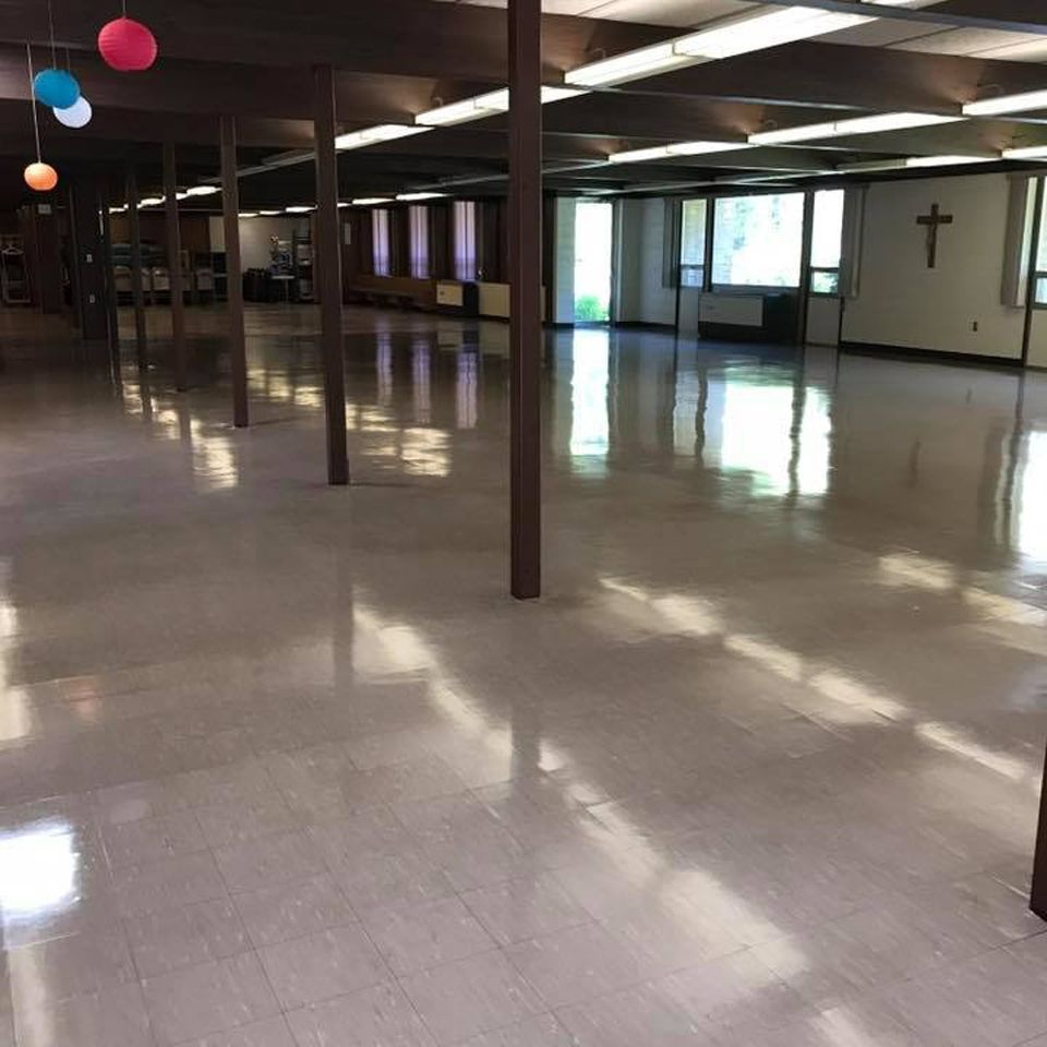 Empty, bright room with shiny floor and dark columns. Windows and a cross are visible.