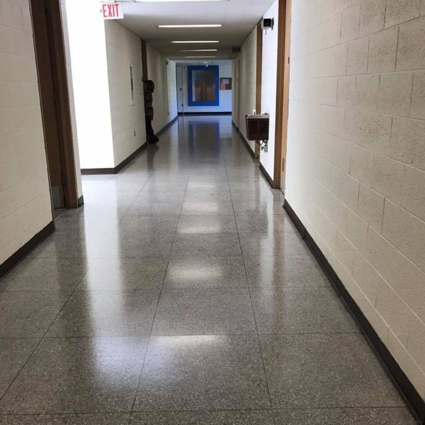 Long hallway with glossy, gray tiled floor. White walls, wooden door frames, and overhead lights.